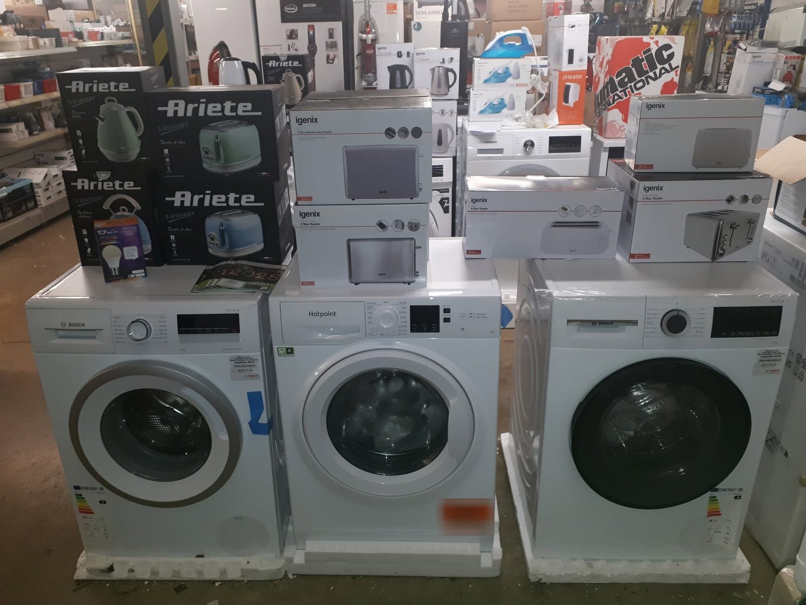 Bosch and Hotpoint washing machines with boxed small appliances stacked on top in the showroom