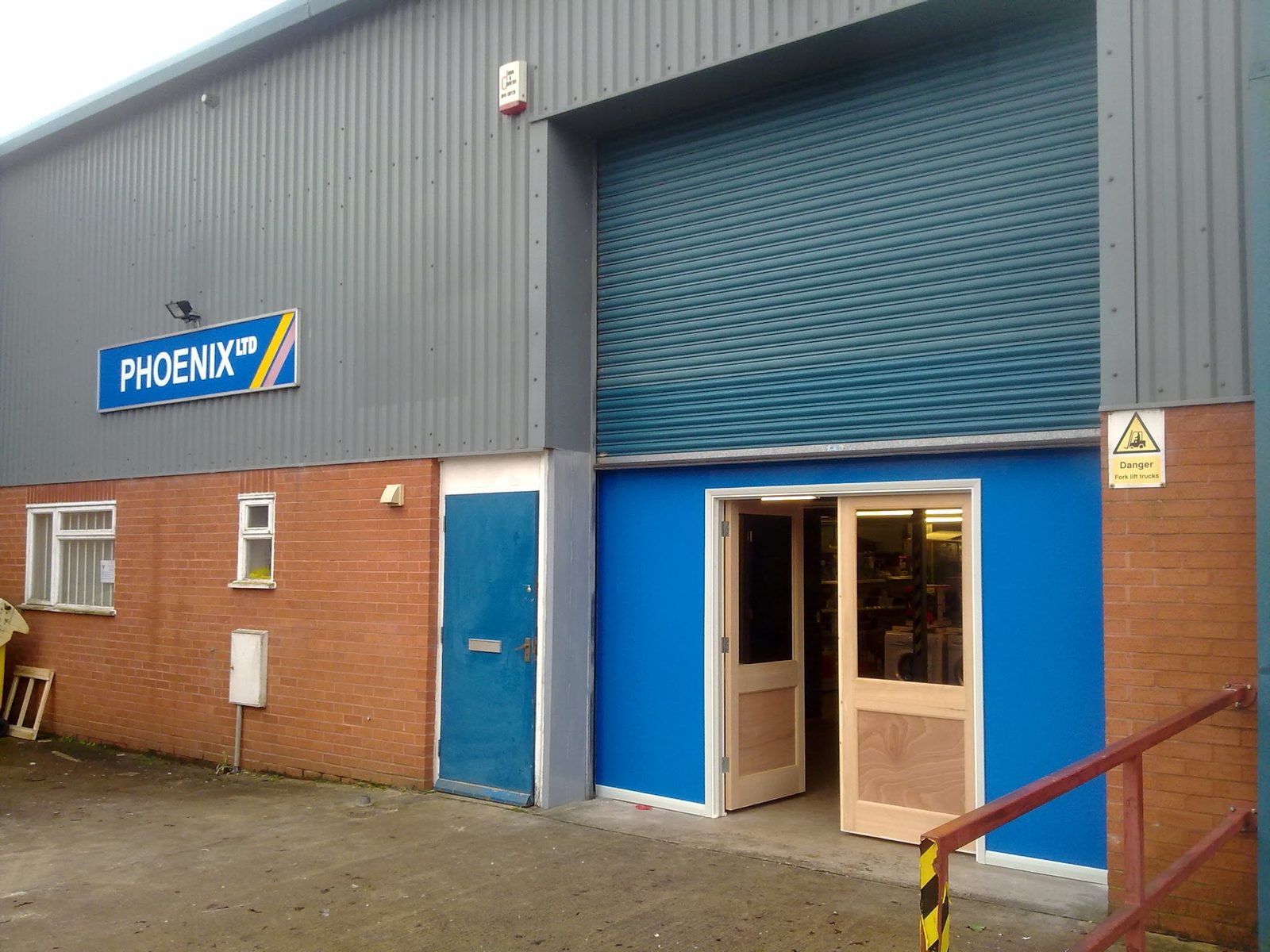 The Phoenix Electrical unit in Station Yard: grey cladding, the blue PHOENIX LTD sign and the open shop doors