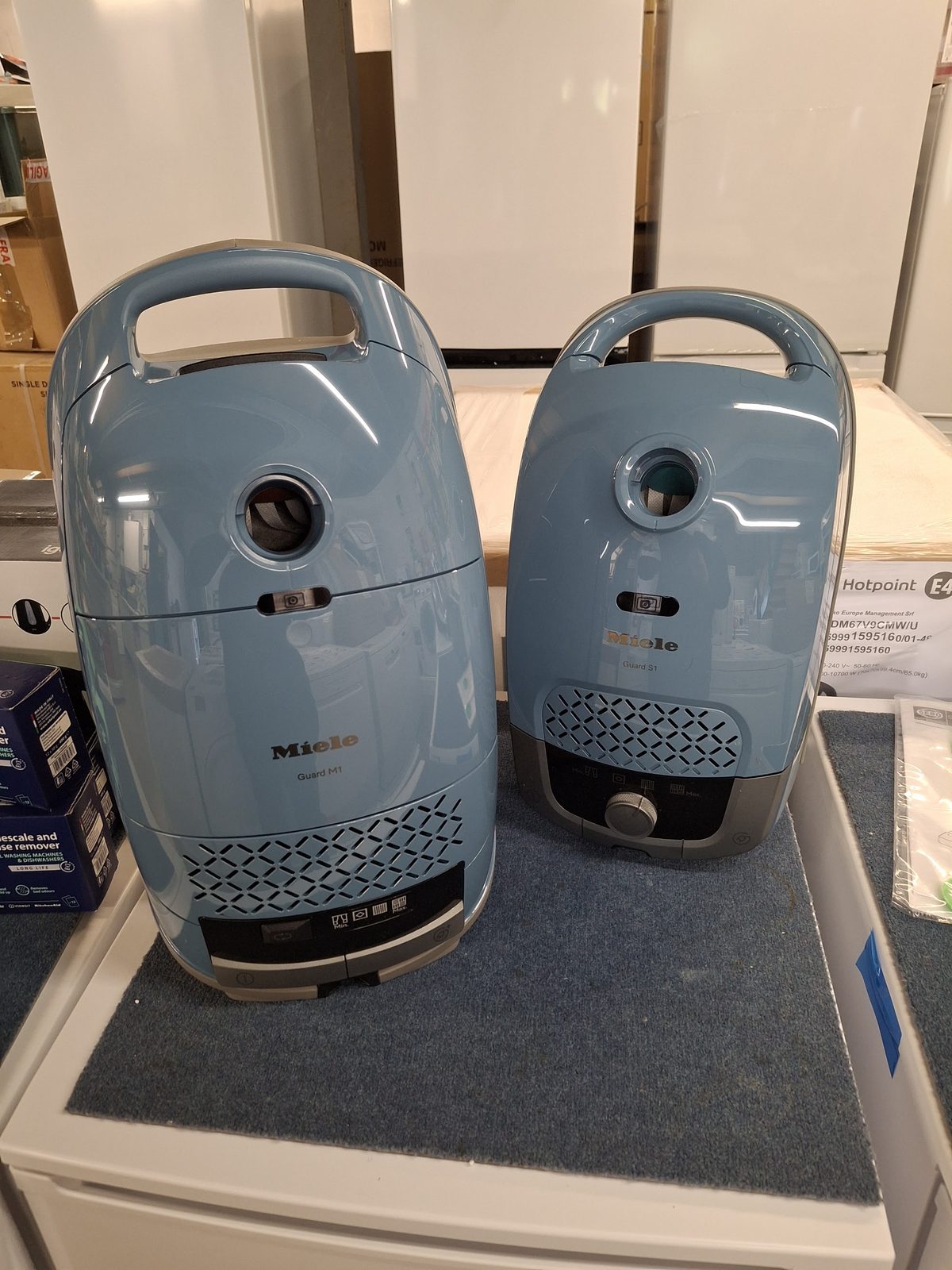 Two pale blue Miele cylinder vacuum cleaners on a display stand